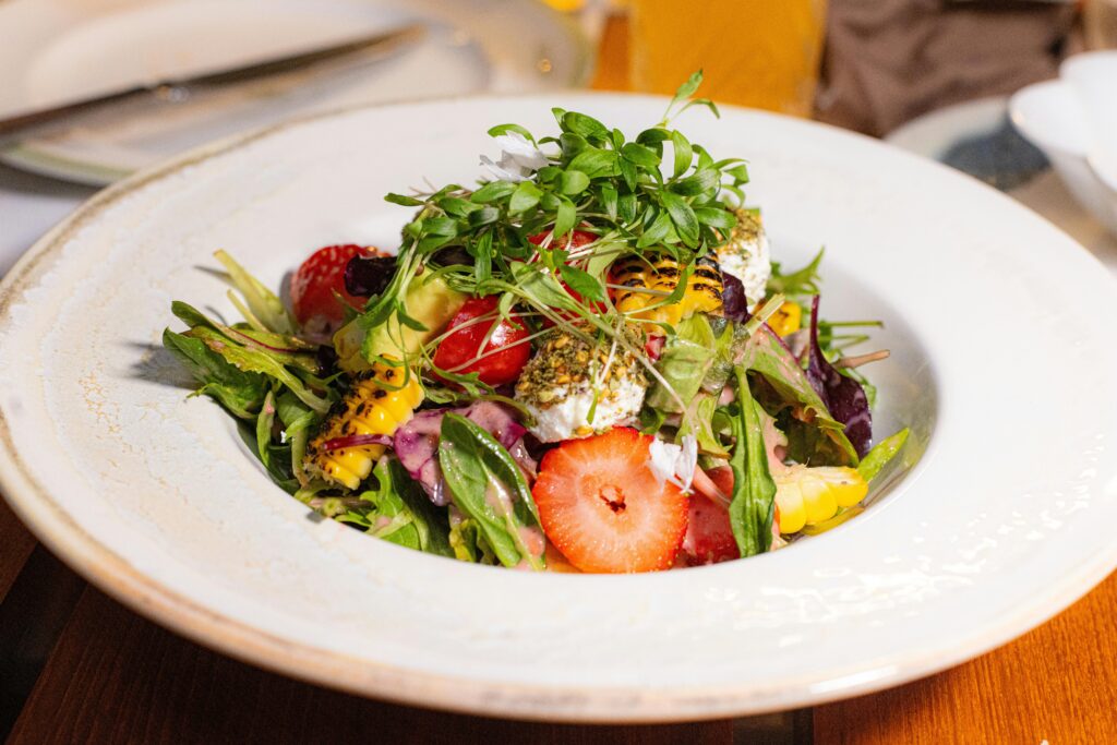 Colorful summer salad with strawberries, greens, and cheese in a white bowl.