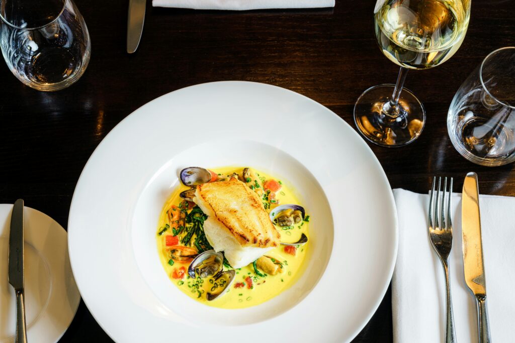 Exquisite seafood dish with clams and fish served at an elegant London restaurant, paired with white wine.